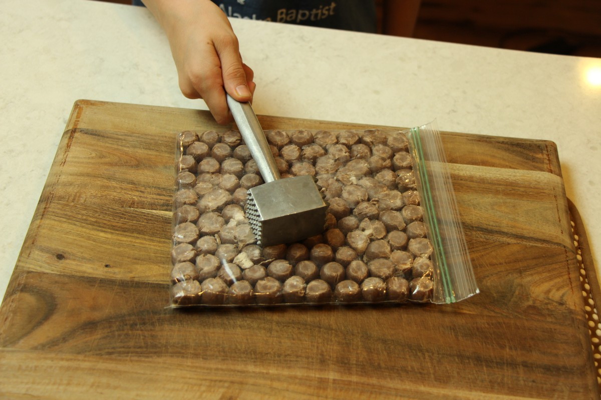 Crushing malted milk balls with meat tenderizer to use in malted milk cookies.