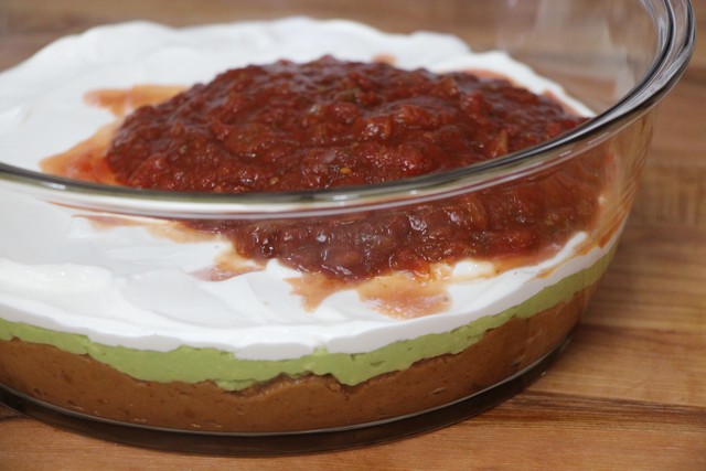 Adding sour cream and salsa to six layer guacamole dip