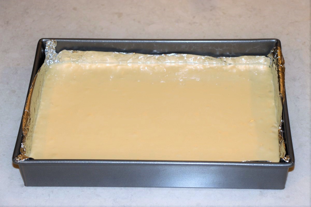 Spreading out filling in cream cheese sticky bars on top of crust. Ready to bake. Recipe.