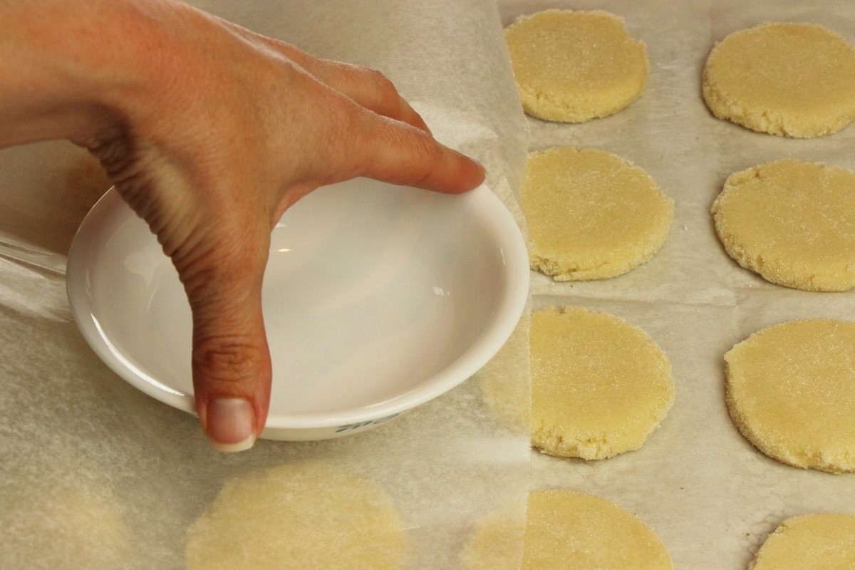 Flattening sugar cookie dough balls using wax paper and flat bowl.