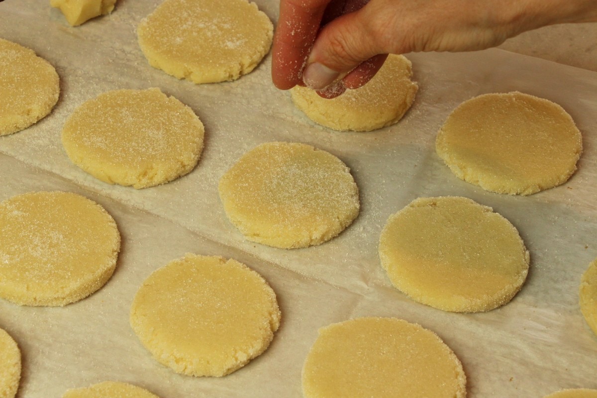 Sprinkling sugar onto flattened sugar cookie dough.